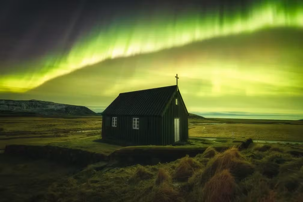 Aurora boreal ao fundo com uma casa mais à frente